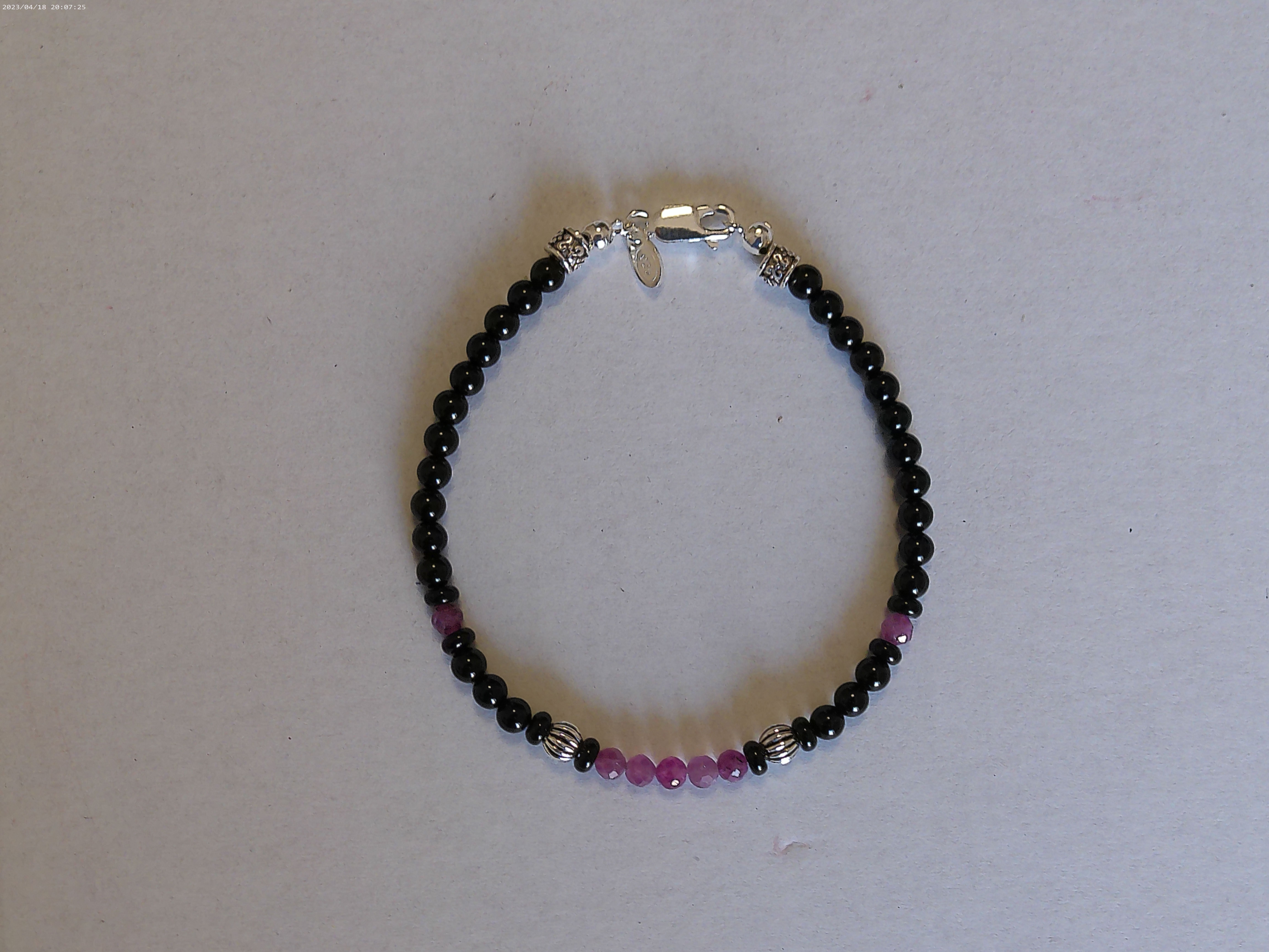 Il bracciale è realizzato con perle di Onice nero e Rubini. Rifinito con accenti in Argento sterling 925 e pratica chiusura a moschettone in Argento sterling 925.
