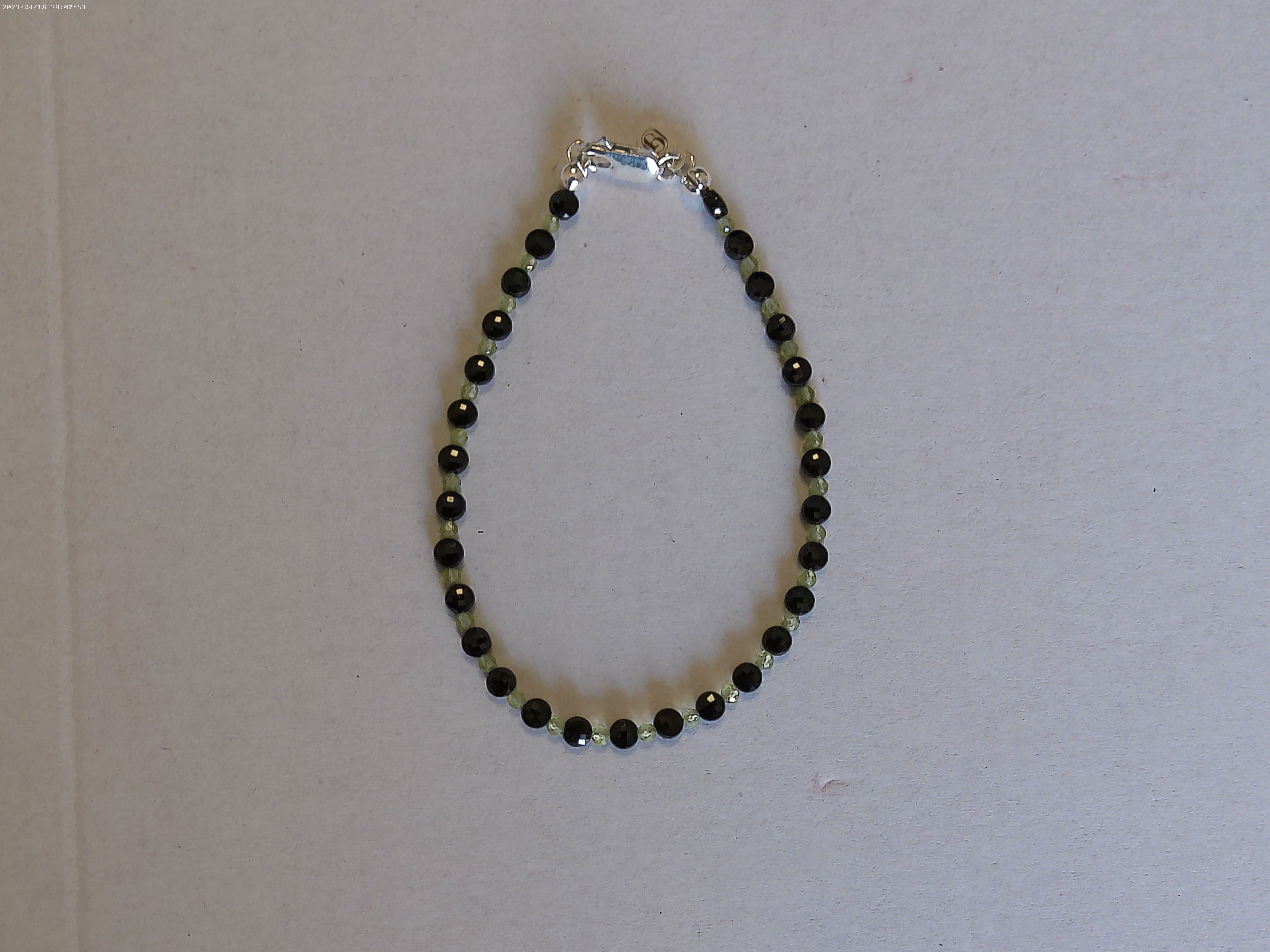 Il bracciale è realizzato con Spinello nero a forma di moneta sfaccettato e Peridoto. Con pratica chiusura a moschettone in Argento sterling 925.